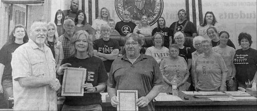 group of men and women standing and smiling in court room holding certificates of proclamation.