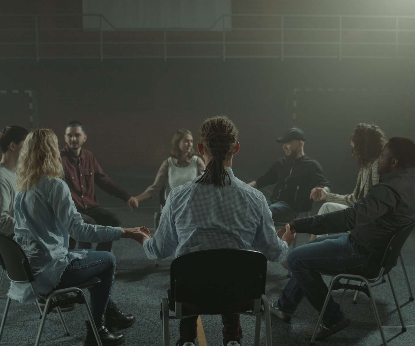 eight persons sit in circle holding hands with careful smiles