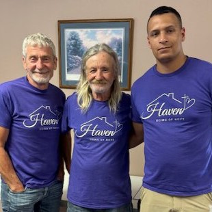 3 men stand close together in a room wearing purple tee shirts with the Haven Home of Hope logo